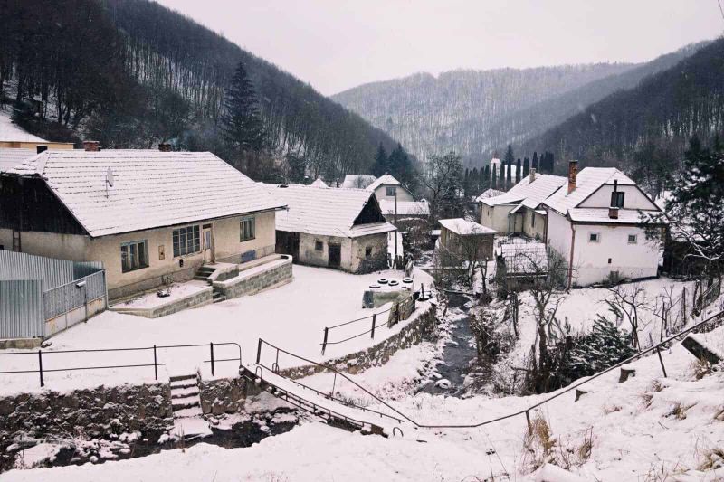 Alloggi accoglienti in montagna per Natale 2 Case di montagna innevate in un paesaggio rurale con boschi e un piccolo corso d'acqua, tutto immerso nella tranquillità della natura invernale in Italia.
