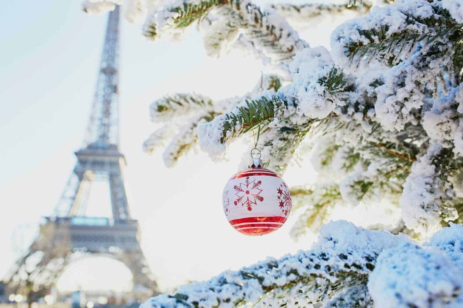 Palla di Natale rossa con fiocco di neve decorativo sull'albero innevato vicino alla Torre Eiffel durante il inverno a Parigi.