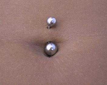 Piercing al ombelico con gioiello a sfera, dettaglio di body art e decorazione della pelle denim.