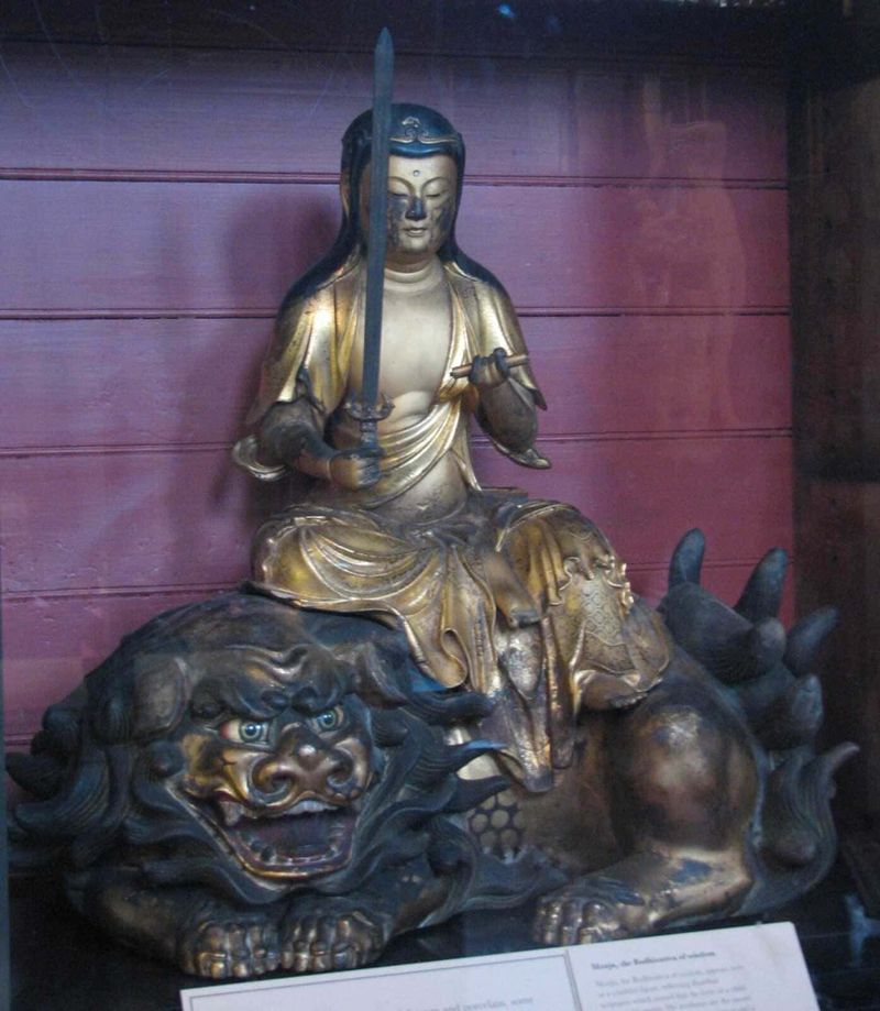 Mitologia buddista: storie di illuminazione e saggezza 5 Futuro, statua di un guerriero orientale in metallo oro e argento con spada e scudo, seduto su un leone di metallo scuro, in una mostra culturale.