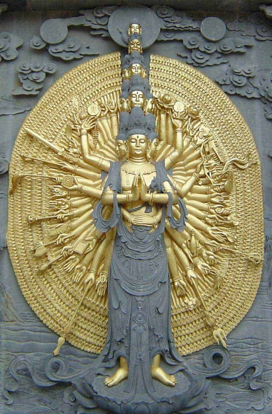 Dettaglio di una statua di Avalokitṣvara, il Bodhisattva della compassione, con molteplici braccia e teste, in stile buddhista asiatico, con superficie dorata e dettagli elaborati.
