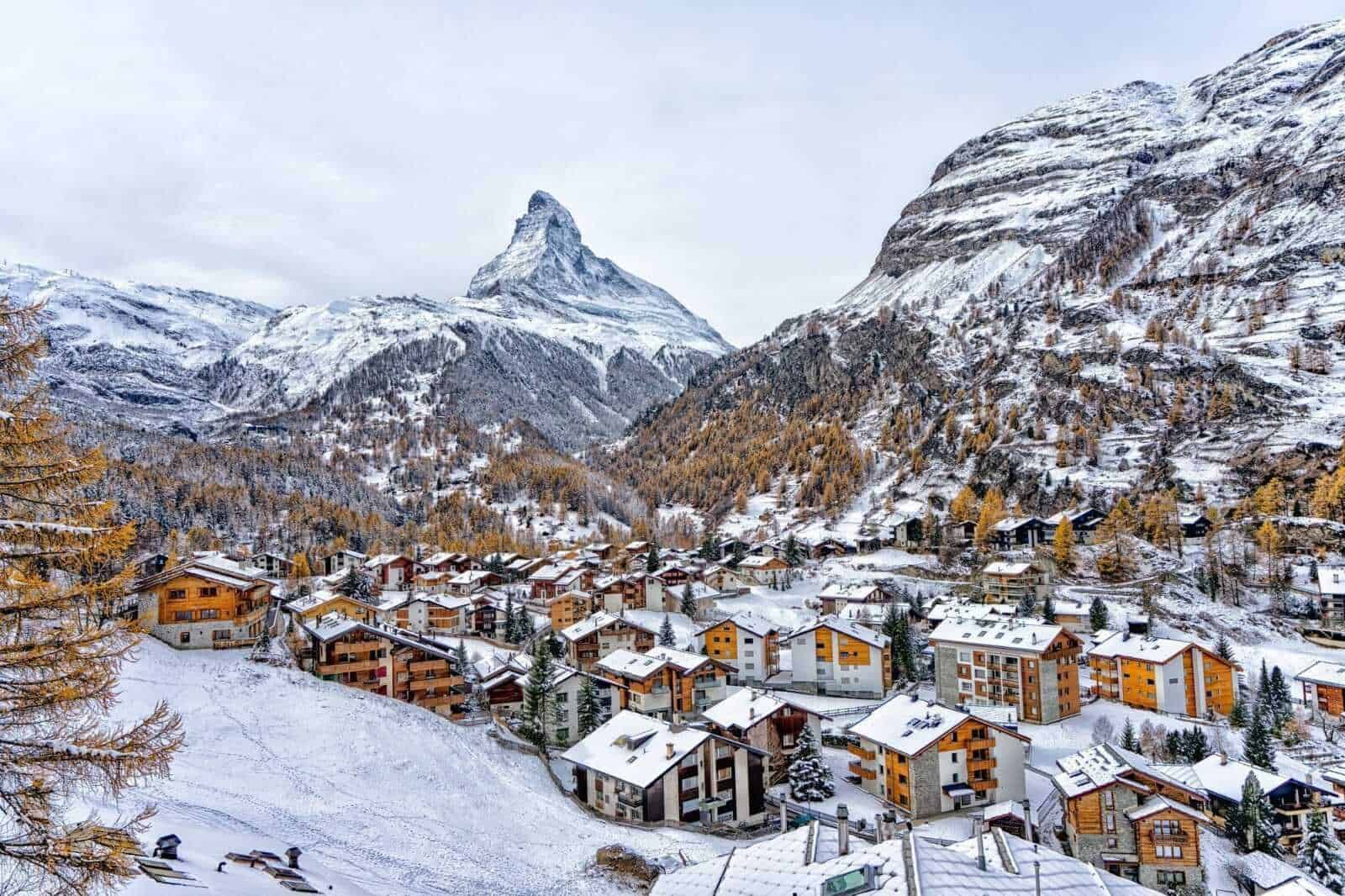 Montagna innevata e villaggi alpini nel paesaggio invernale, con il famoso Monte Cervino visibile all'orizzonte, durante una giornata nuvolosa, rappresentando le scogliere e le case di montagna.