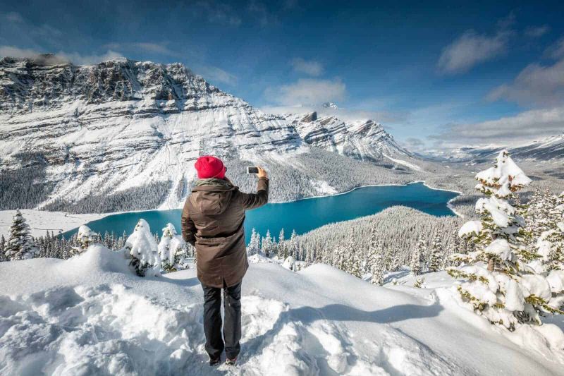 5 destinazioni innevate per il Natale in montagna 6 L'altimetria di una persona che scatta una foto al lago ghiacciato circondato da montagne innevate.