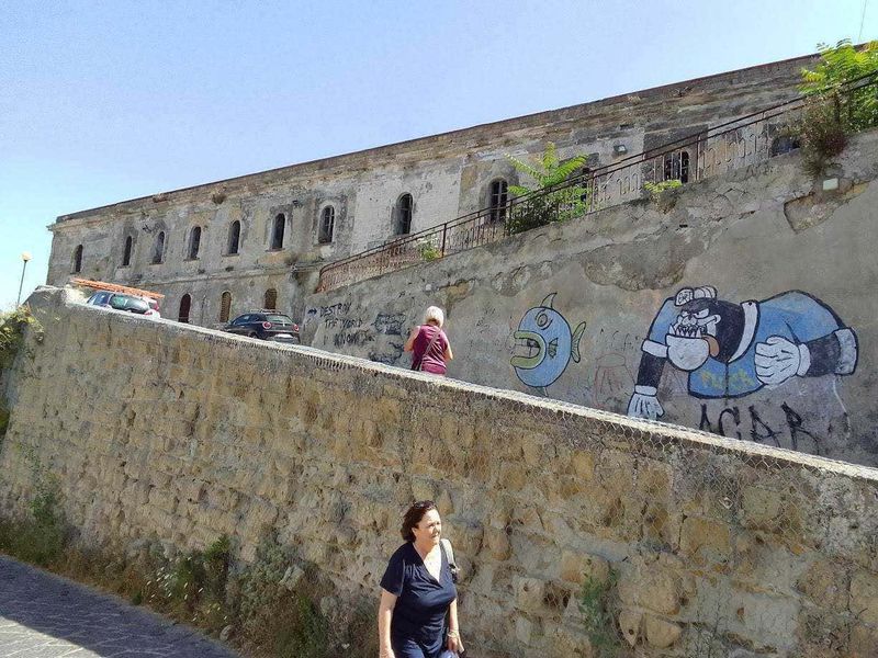 Procida: isola dei pescatori e cultura 6 Colorata street art graffiti su muro di pietra antico con persone che passeggiano, scenario urbano storico e moderno, wall art creativa, ambiente cittadino, arte urbana.