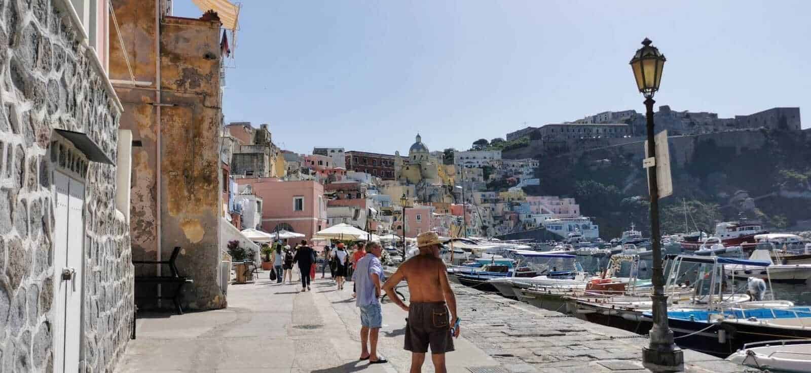 Barca di molo con yacht e case colorate sullo sfondo nel Porto di Positano, Italia, durante una giornata soleggiata, con turisti che passeggiano lungo il lungomare.