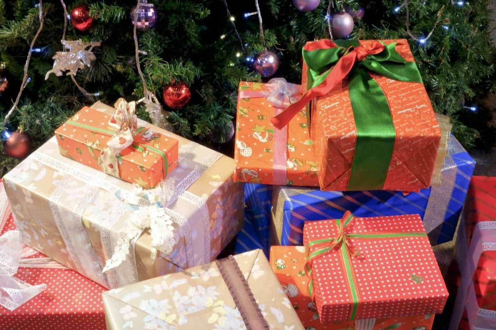 Pacchi regalo natalizi sotto l'albero di Natale decorato con luci e palline colorate, perfetti per le festività e lo scambio di doni durante il periodo natalizio.