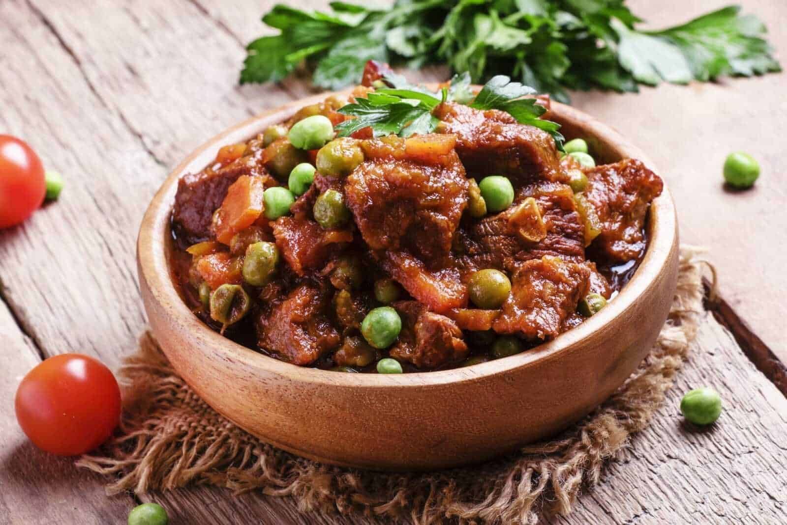 Ricetta di stufato di carne con piselli in ciotola di legno, ingrediente tradizionale italiano, pasto sostanzioso e ricco di sapore, cucina fatta in casa con verdure fresche e carne di qualità.