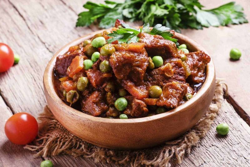 Tradizioni natalizie uniche in montagna 3 Ricetta di stufato di carne con piselli in ciotola di legno, ingrediente tradizionale italiano, pasto sostanzioso e ricco di sapore, cucina fatta in casa con verdure fresche e carne di qualità.