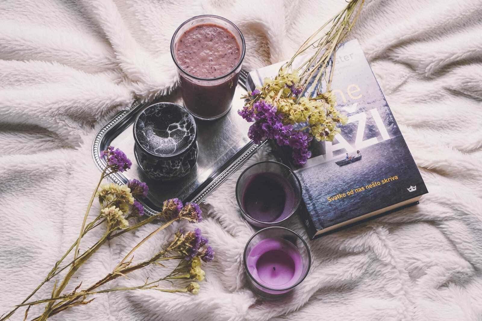 Un servizio di tocco retrò con bevande colorate, fiori secchi e un libro, tutto disposto su una coperta morbida, creando un ambiente accogliente e rilassante per una pausa di lettura e relax.