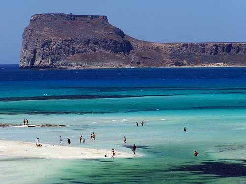Spiaggia di sabbia bianca con acque turchesi e scogliera imponente sullo sfondo, ideale per turismo e relax in natura in un paradiso mediterraneo.