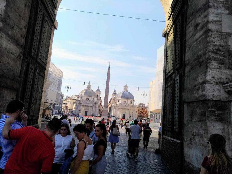 18 luoghi Conte di Montecristo a Roma 6 Passeggiata nel cuore di Roma con vista su Piazza del Popolo, le chiese gemelle e l'obelisco nel centro, tra turisti e cittadini che ammirano l'arte e la storia della città eterna.