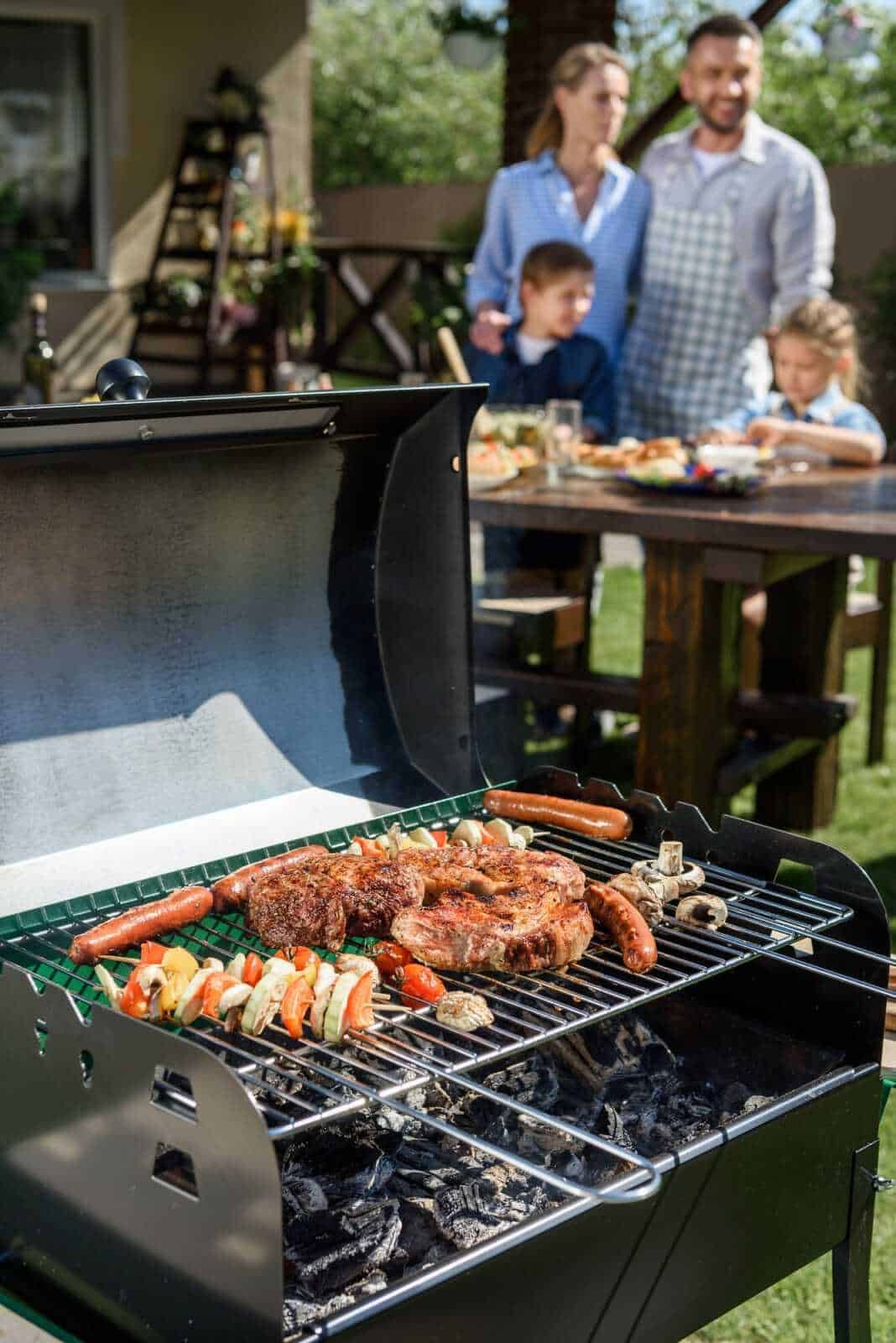 Carne alla griglia con verdure miste di contorno, famiglia felice che prepara un barbecue all'aperto in giardino, estate, picnic, cibo all'aperto.