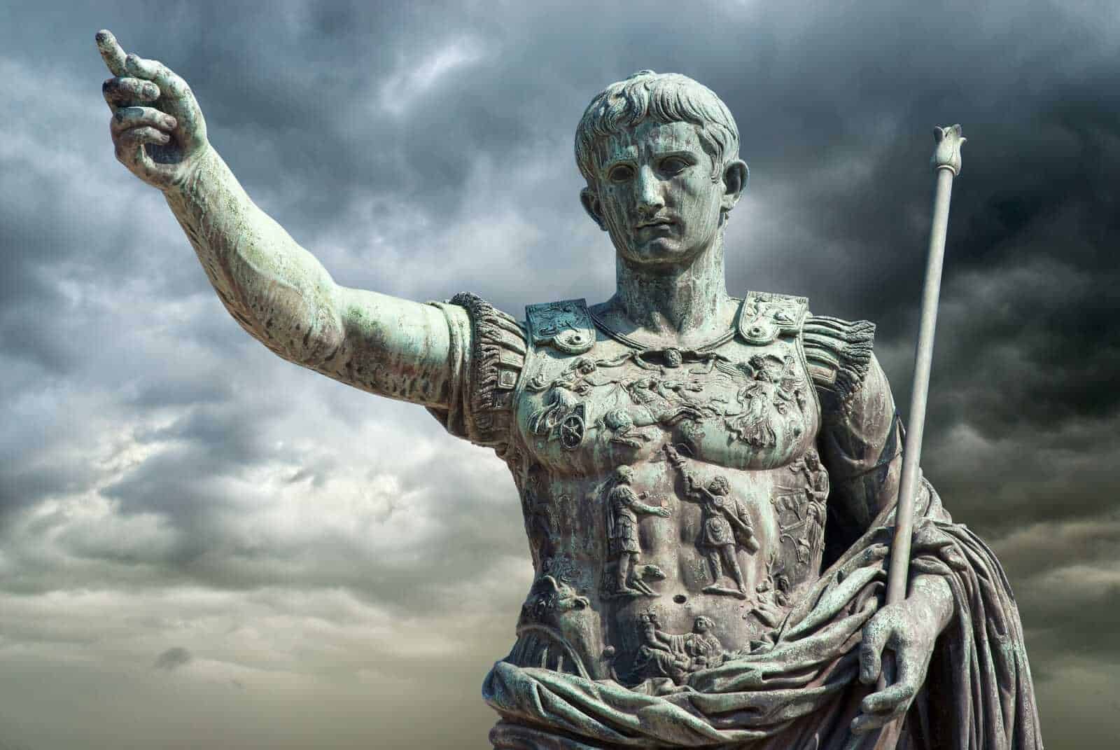 Antica statua di un imperatore romano in bronzo con dettagli e sculture elaborati, sotto un cielo nuvoloso, simbolo di potere e storia antica.
