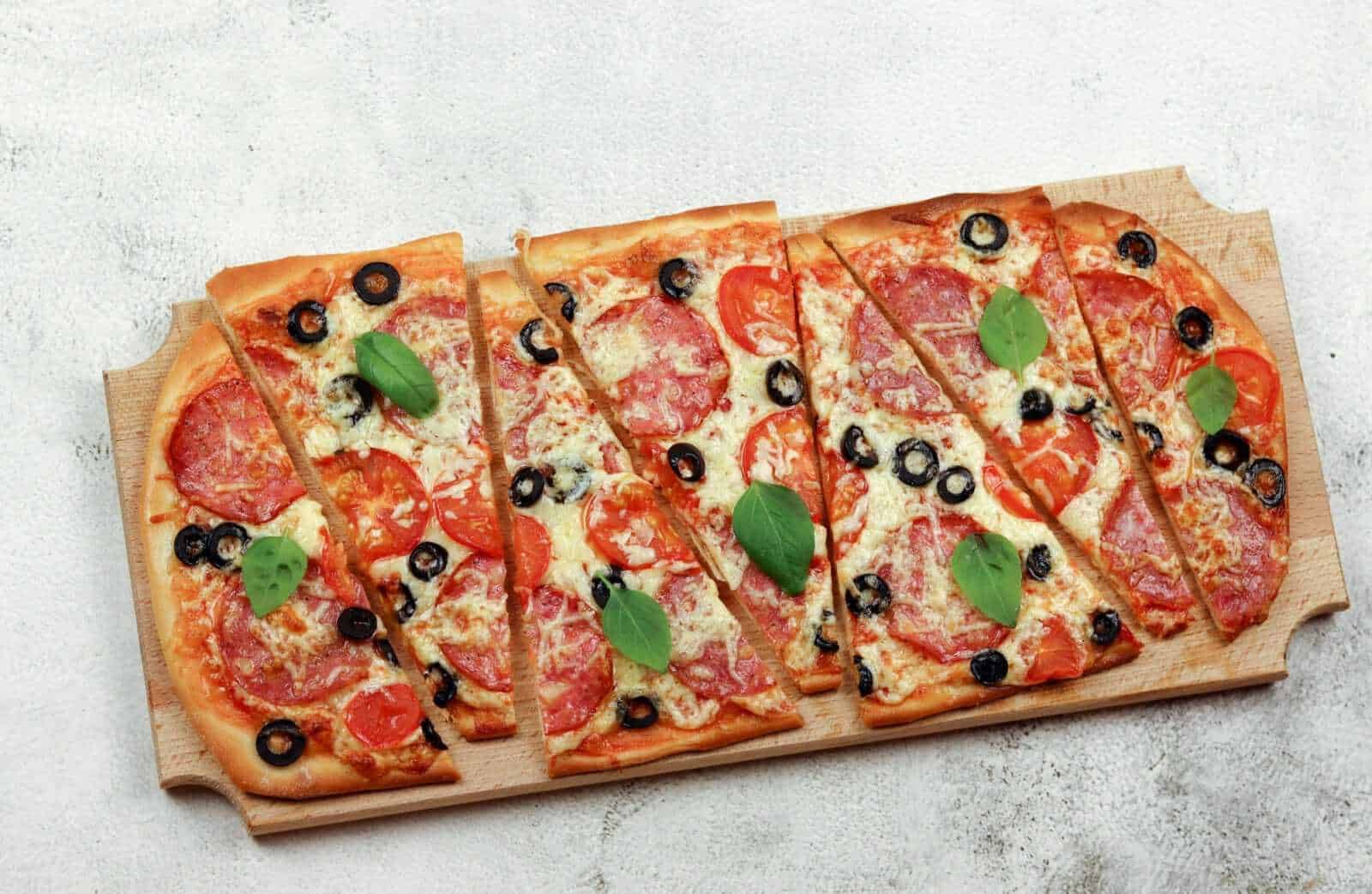 Fetta di pizza margherita farcita con pomodoro, mozzarella, olive nere, basilico fresco su tavola in legno.