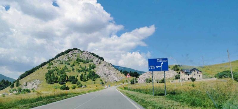 Parco Nazionale della Majella, 12 attrazioni in Abruzzo 2 Montagna verde con strada di campagna e segnaletica stradale in Italia, paesaggio naturale e cielo azzurro.