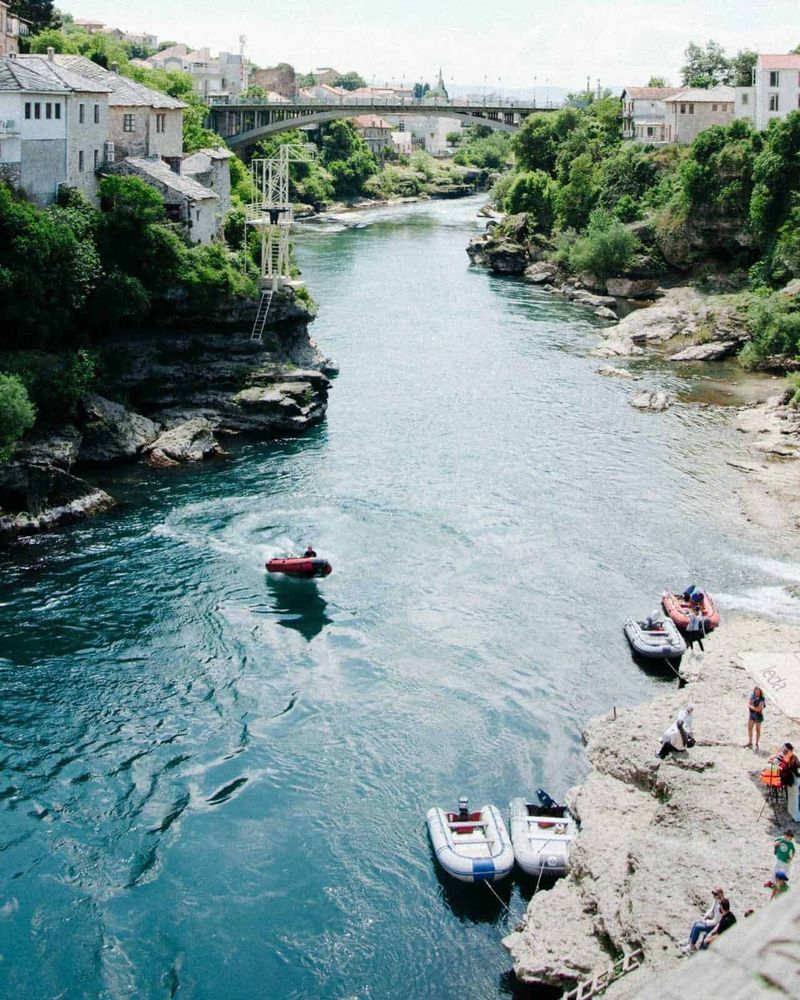 Le Migliori Destinazioni per il Rafting 3 Lago Ilissos a Potenza, con barche in acqua e falesia con persone che si rilassano, circondato da case e vegetazione, in una giornata di relax e attività all'aperto nel cuore della città.