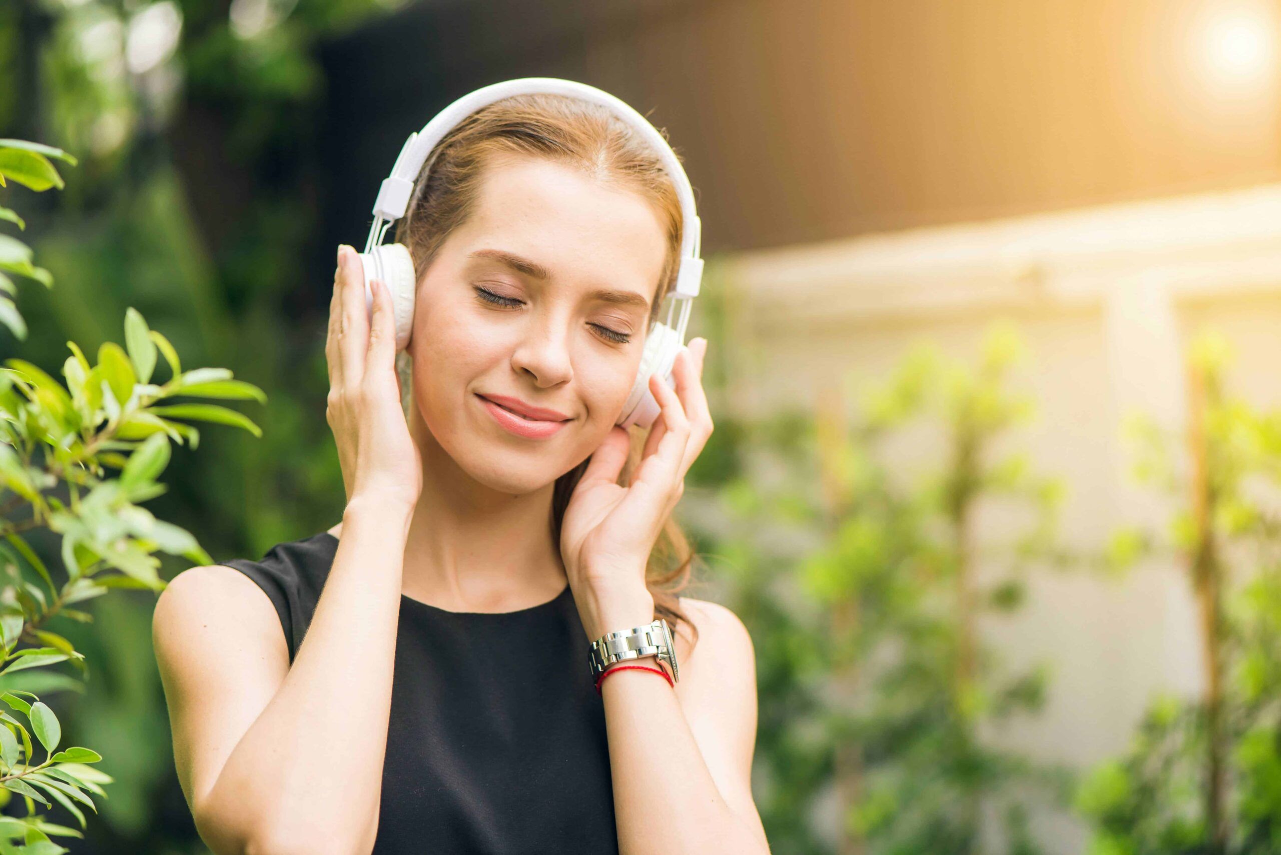 Musica e relax all'aperto: donna che ascolta musica con cuffie in natura, ambiente verde e solare, perfetto esempio di benessere e ascolto musica relax all'aperto.