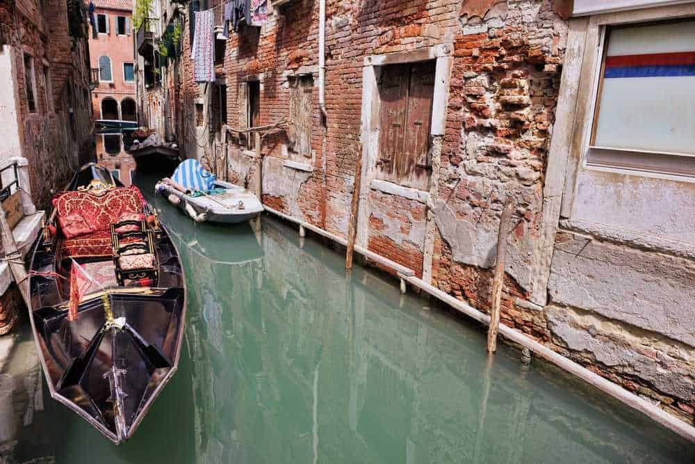Barche ancorate in un canale di Venezia, con edifici storici e facciate in mattoni visibili lungo il bordo dell'acqua, rappresentando il caratteristico paesaggio veneziano.