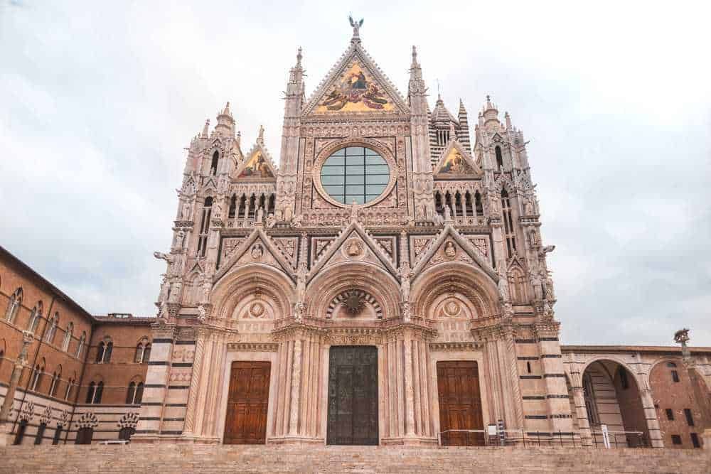Maestosa facciata della Cattedrale di Siena in stile gotico, con dettagli architettonici elaborati e facciata decorata, simbolo di arte e storia italiana. Ricca di elementi storici e culturali, rappresenta un'icona religiosa e artistica del patrimonio italiano.
