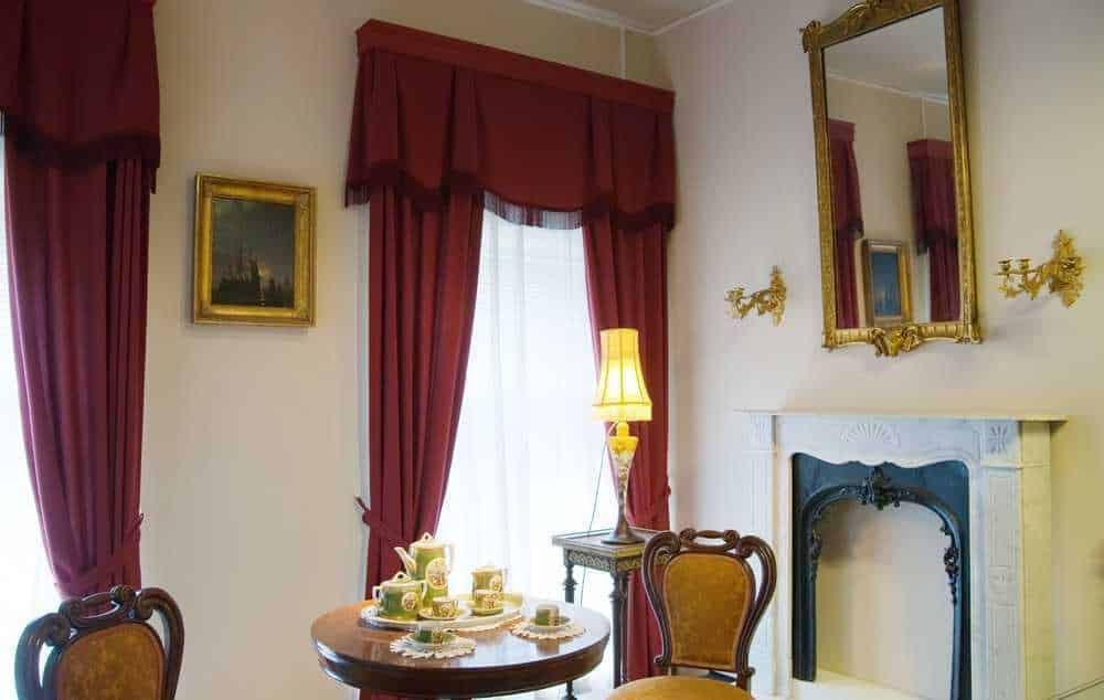 Elegante sala con tende rosse, camino decorativo e specchio dorato, ideale per un ambiente raffinato e accogliente. Dettagli classici e decorazioni vintage che creano un'atmosfera calda e raffinata.
