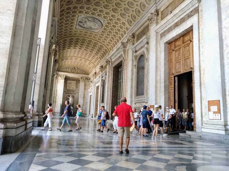 15 Attrazioni vicine alla Basilica di San Pietro 9 Immagine di un grande salone storico con soffitto decorato e pareti in marmo, visitato da un gruppo di turisti che osservano le opere d’arte e l’architettura elegante, perfetta per appunti sul blog di viaggi e cultura.