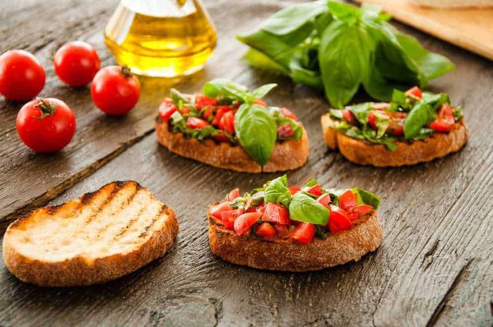 Pomodori freschi e bruschette con pomodoro e basilico su tavola di legno, ingrediente tipico della cucina italiana. Ricetta semplice e gustosa con prodotti di qualità, ideale per un antipasto o uno spuntino salutare.