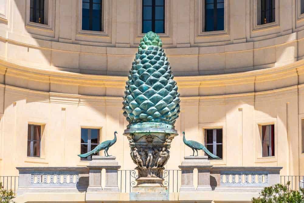Pineta di libri di arte e cultura, statua decorativa di pigna con uccelli, simbolo di natura e spiritualità, ideale per appassionati di arte, storia e cultura italiana, ambiente accattivante e ricco di fascino.