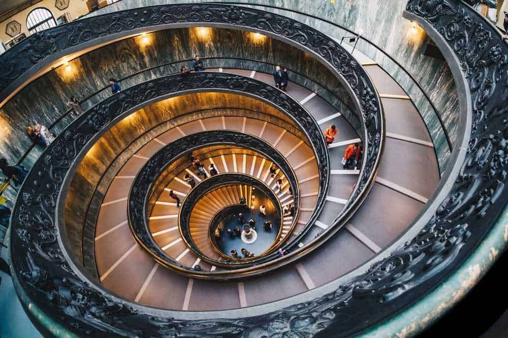 Attrazioni vicino alla basilica di san pietro: Elegante scalinata a spirale di un museo con dettagli artistici in ferro battuto e luci calde. Scenario mozzafiato che unisce arte, architettura e design per un'esperienza visiva unica.