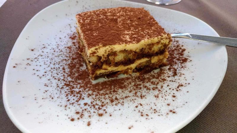 Tiramisù al limoncello per amanti sapori agrumati 3 Delicious homemade tiramisu dessert on a white plate with cocoa powder topping, served with a fork; perfect for coffee and dessert lovers, ideal for Italian cuisine.