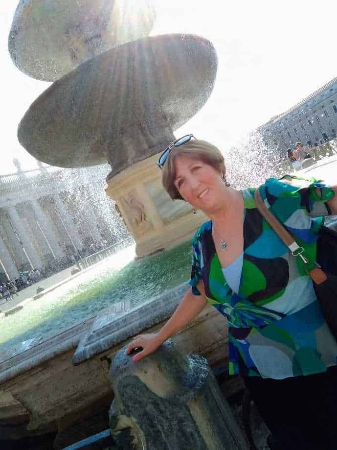 Fonte di acqua verde in stile classico con donna sorridente e occhiali da sole vicino a una fontana storica a Piazza Navona, Roma.