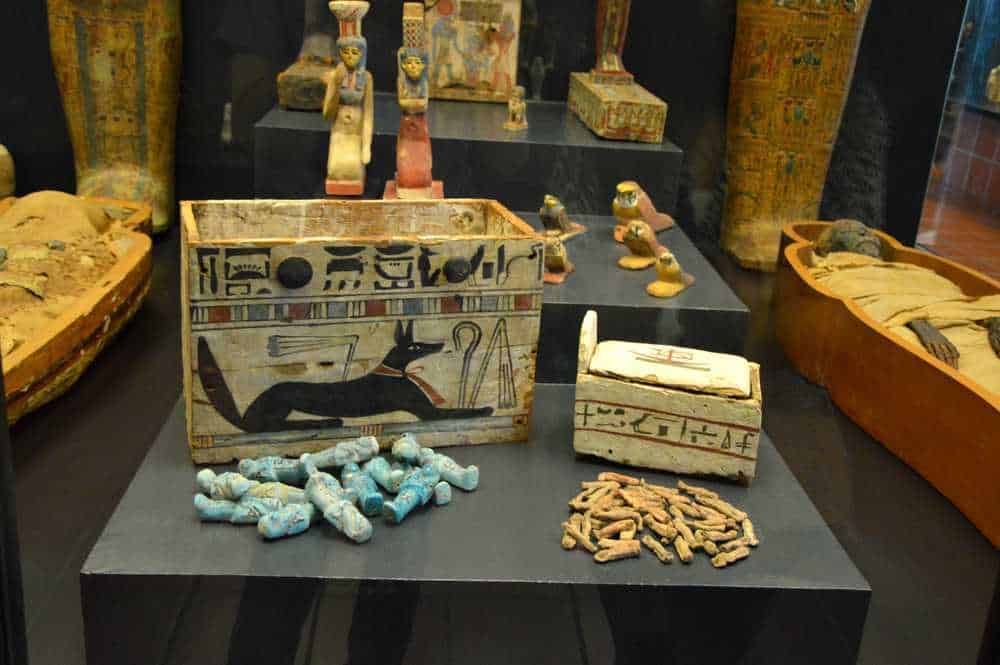 Antico reperto archeologico egizio con sarcofagi, amuleti e iscrizioni geroglifiche, cimeli museali per appassionati di storia antica e cultura egizia.