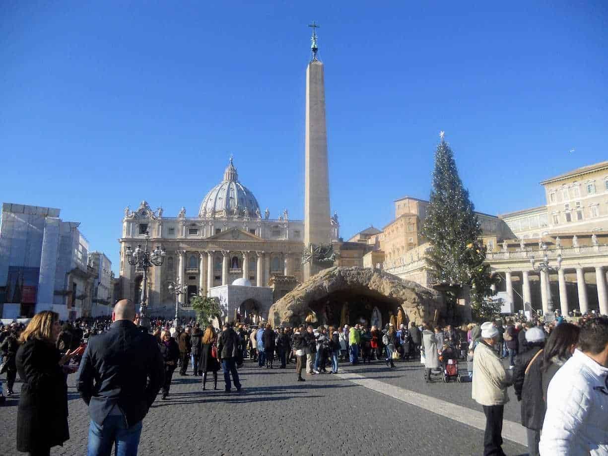 Piazza San Pietro a Roma con il grande albero di Natale, il presepe e la basilica di San Pietro in sottofondo, durante il periodo natalizio, con molti visitatori presenti.