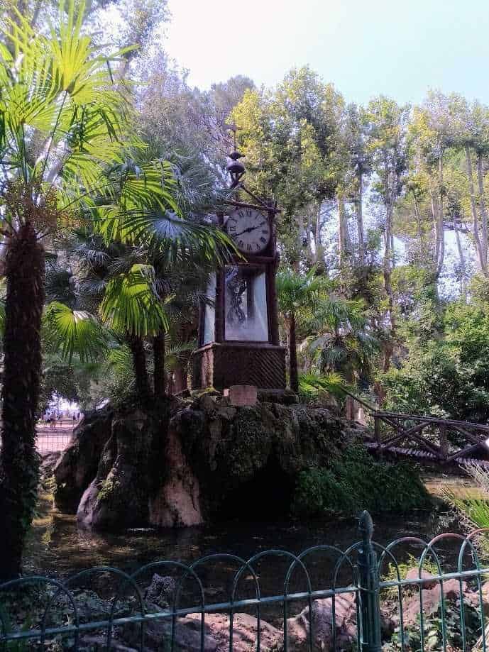 Orologio idraulico del pincio a roma: Vecchietto in un parco con orologio di vetro e tetto di paglia, sorridente con cappello e occhiali da sole alla moda, in un ambiente verde lussureggiante, perfetto per esplorare la natura e scattare foto ricordo.