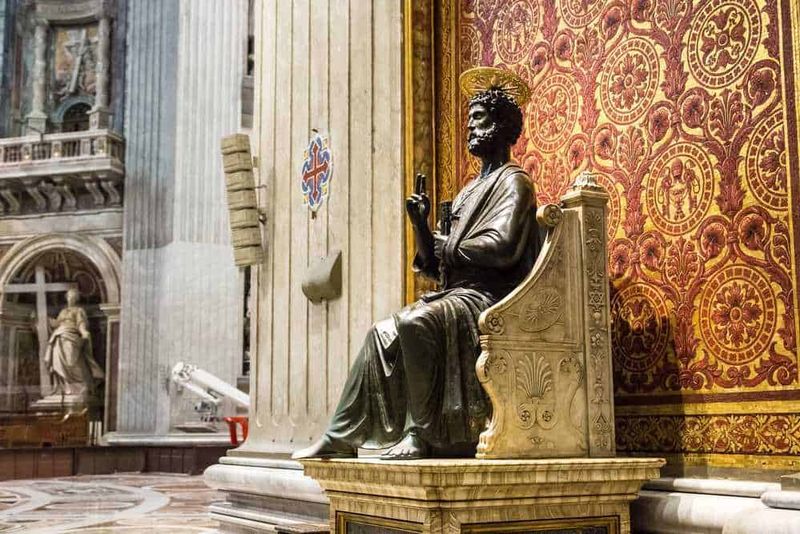 Basilica di San Pietro: Storia e Segreti 9 Statuetta di San Paolo in bronzo all'interno di una chiesa storica con dettagli decorativi dorati e pareti con tessitura elaborata, simbolo di fede e arte sacra.