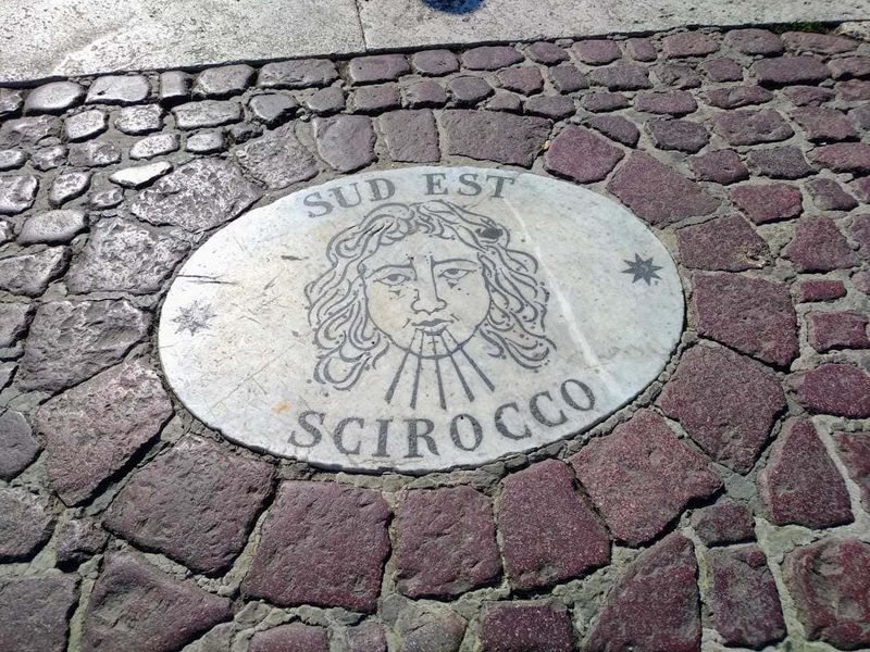 7 Cose da vedere in Piazza San Pietro gratis 8 Sud Est Scirocco manhole cover su strada cittadina, elemento di design urbano con decorazioni artistiche e testi.