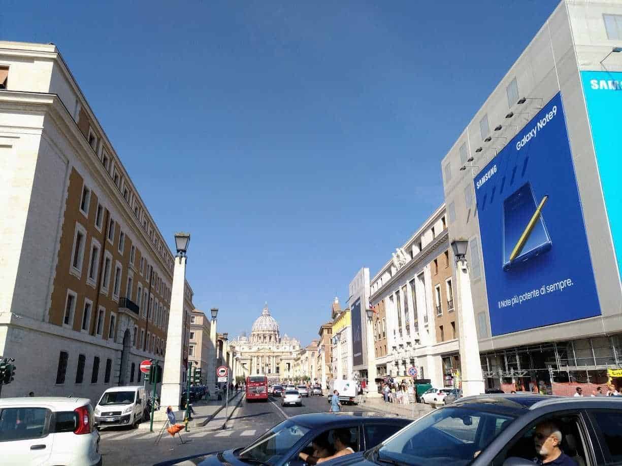 Samsung Galaxy Note9 pubblicità gigante su edificio storico a Roma, vista strada trafficata con cittadini e auto, alla scoperta di luoghi iconici della città eterna.