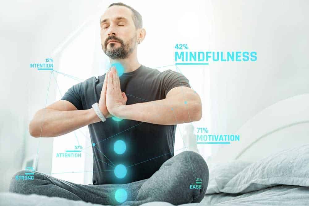 Ritratto di un uomo che medita in posizione di yoga, appoggiato su un letto, con grafici di benessere mentale e concentramento, concetto di mindfulness, attenzione, motivazione e easiness.