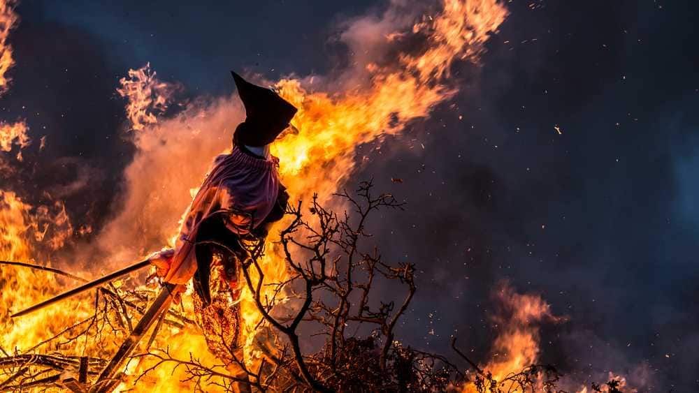 Brusca scena di un pagliaccio che sprezza un rogo alimentato dalle fiamme e dal fumo denso contro un cielo scuro, simbolo di paura e distruzione, ideali per articoli sulla paura, i miti o gli incidenti.