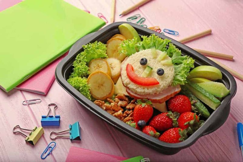 Idee per lunch box bambini sani e nutrienti 3 Sano pranzo in contenitore con faccina fatta di alimenti freschi, frutta e verdura, ideale per i pasti dei bambini.