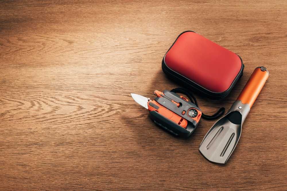 Multitool compatto con lama, torcia e cassetta di pronto soccorso su superficie in legno. Strumenti multifunzione per outdoor, campeggio e emergenze.