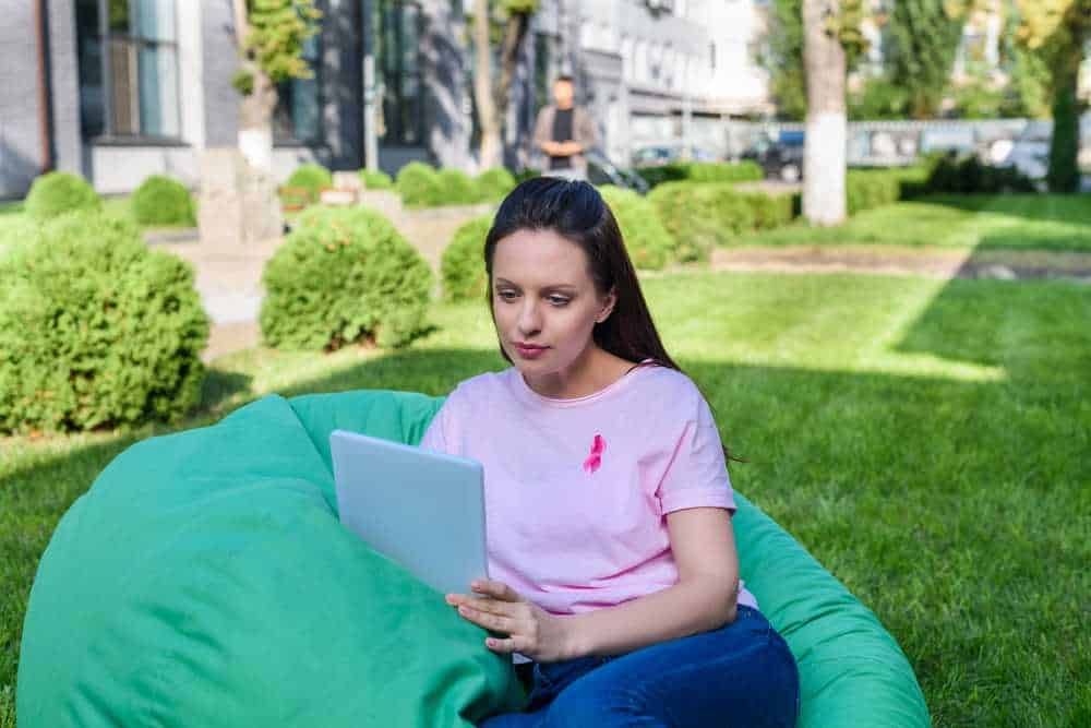 Notebook aperto su un prato verde con donna che utilizza un dispositivo digitale in un ambiente esterno.