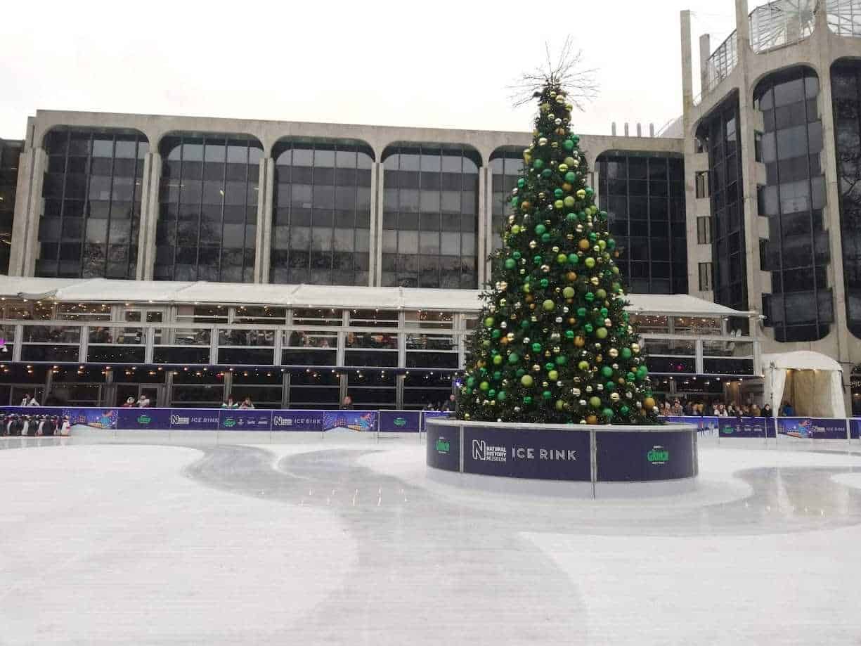 Altre testo_alt: Albero di Natale decorato con palline verdi e oro in una pista di pattinaggio sul ghiaccio all'aperto durante le festività natalizie a Milano.