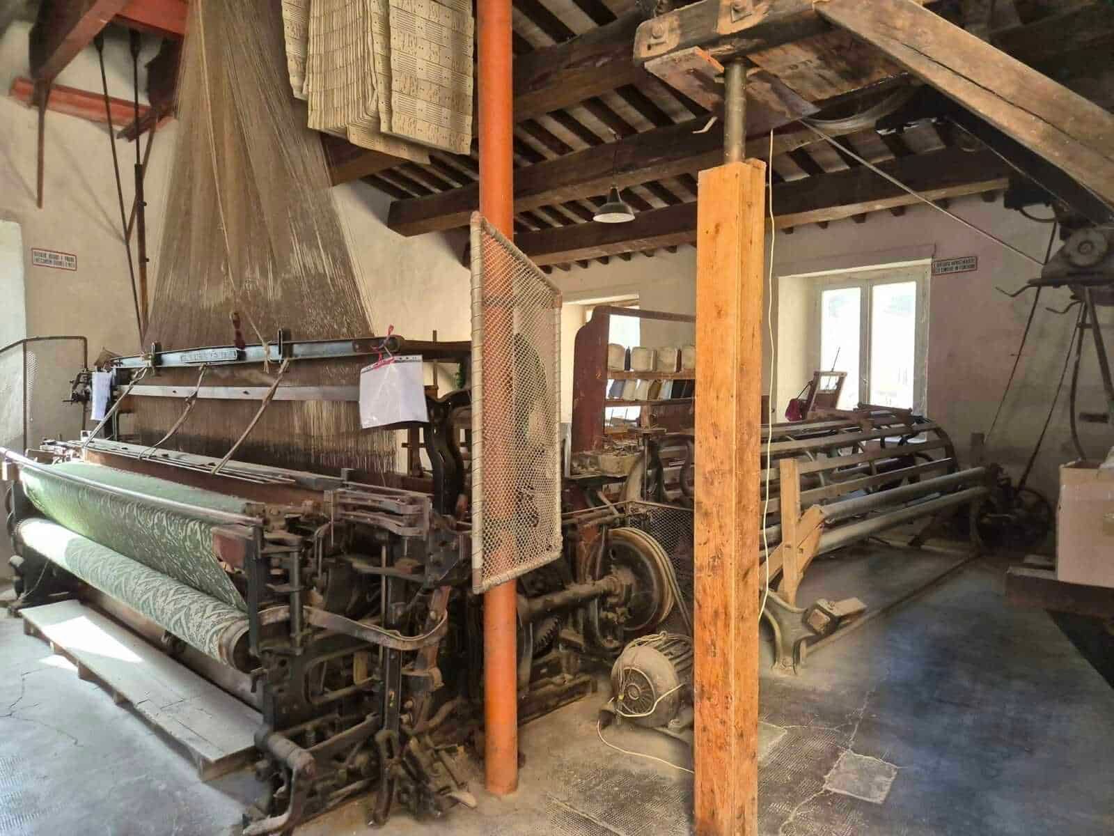 Macchina tessile vintage in un laboratorio artigianale con travi in legno e macchinari typici, ambientazione rustica, ideale per immagini di produzione tessile tradizionale, artigianato e storia industriale.