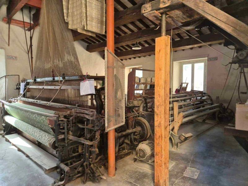 Rasiglia Umbria: Where It Is Located and What to See 5 Macchina tessile vintage in un laboratorio artigianale con travi in legno e macchinari typici, ambientazione rustica, ideale per immagini di produzione tessile tradizionale, artigianato e storia industriale.