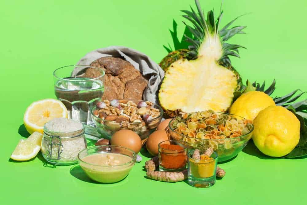 Pineapple, limoni, uova, farina, pasta, biscotti, e spezie su sfondo verde, simbolo di ingredienti freschi per ricette e cucina naturale.