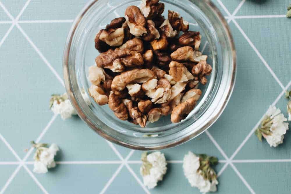 Noci sgusciate in barattolo di vetro su tavolo con fiori bianchi, ingredienti naturali per ricette e snack salutari, alimentare, biologico.