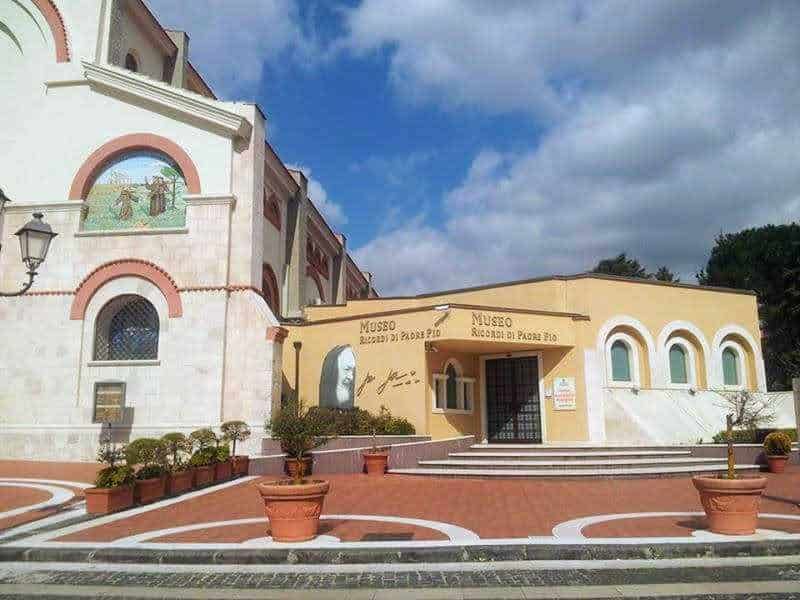 Museo di arte e storia a Padula, facciata colorata con piante in vaso, ingresso principale con scale, cielo nuvoloso, edificio storico e culturale in stile mediterraneo.