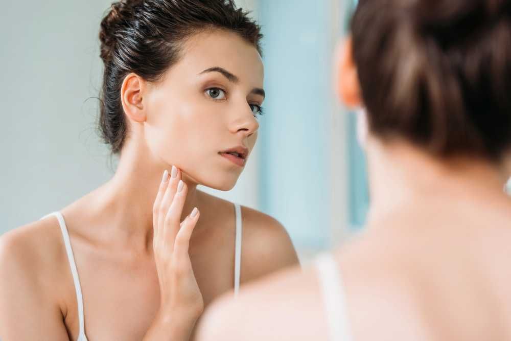 Pelle giovane e luminosa, donna che si prende cura del viso davanti allo specchio, routine di skincare, bellezza naturale, trattamento viso.