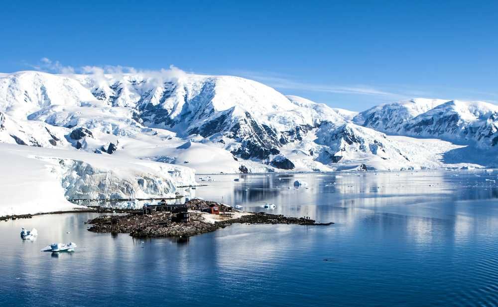Montagne innevate e ghiacciai nell'Antartide con acque cristalline e iceberg galleggianti, paesaggio glaciale unico e spettacolare.