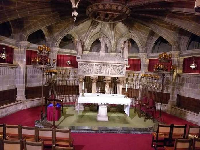 La cattedrale di Barcellona si chiama Santa Eulalia 3 Alt: Interno di una chiesa storica con altare, pareti in pietra, sedili in legno e illuminazione artistica.
